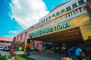 Fachada del Grand Palace Hotel con entrada despejada, un árbol de Navidad y una zona de estacionamiento.