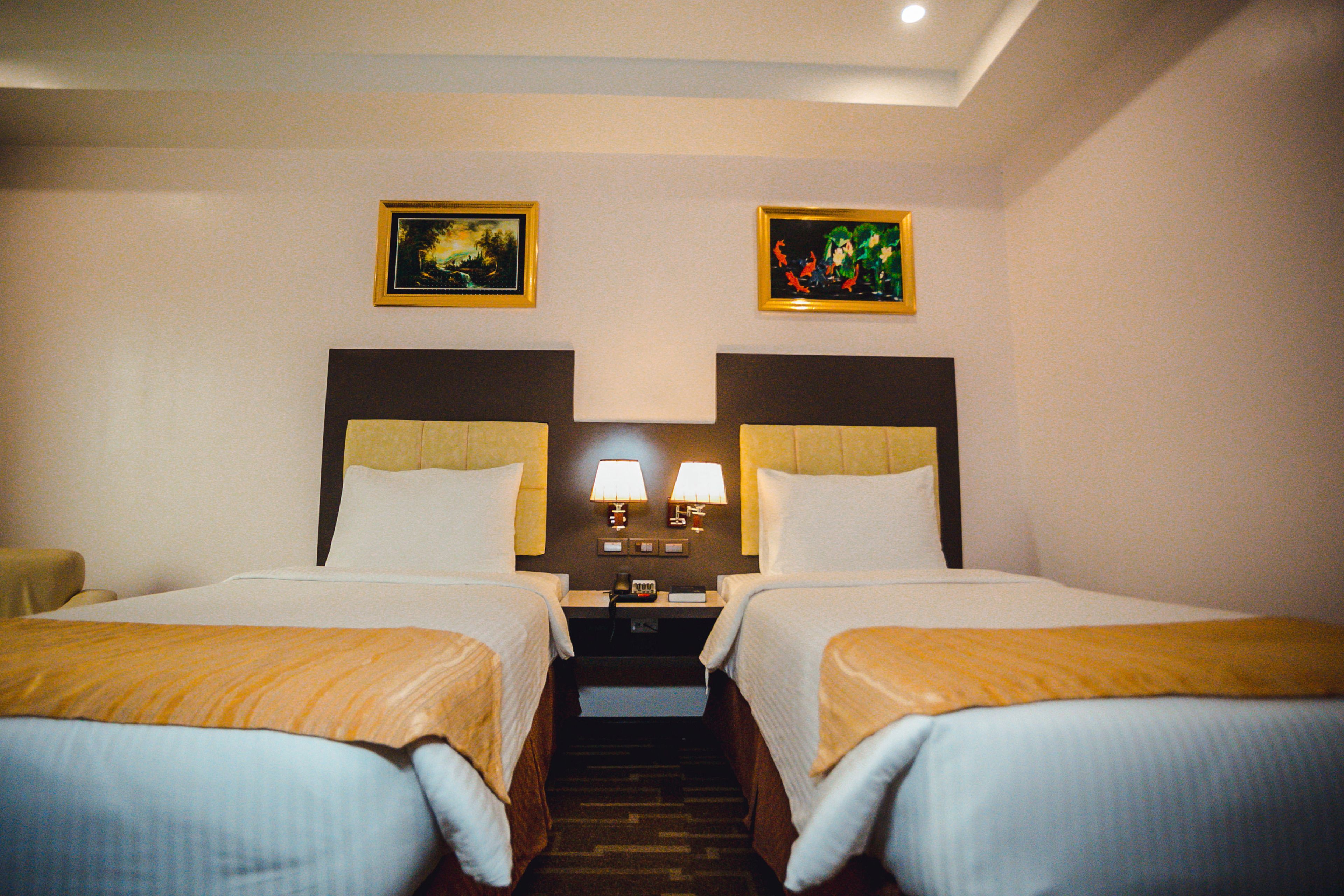 A hotel room with two beds, a nightstand with lamps, and two framed pictures on the wall.