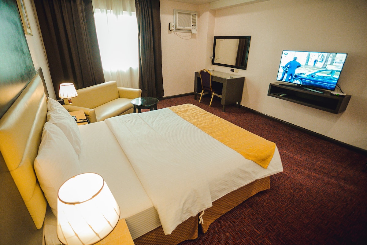 A hotel room with a bed, a desk, a chair, a television, and a lamp.