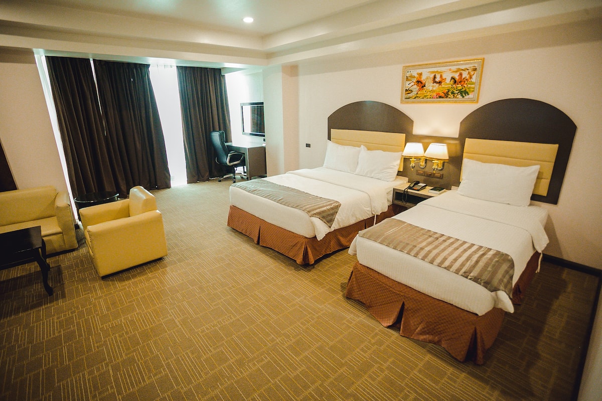 A hotel room with two beds, a desk, a chair, and a painting on the wall.