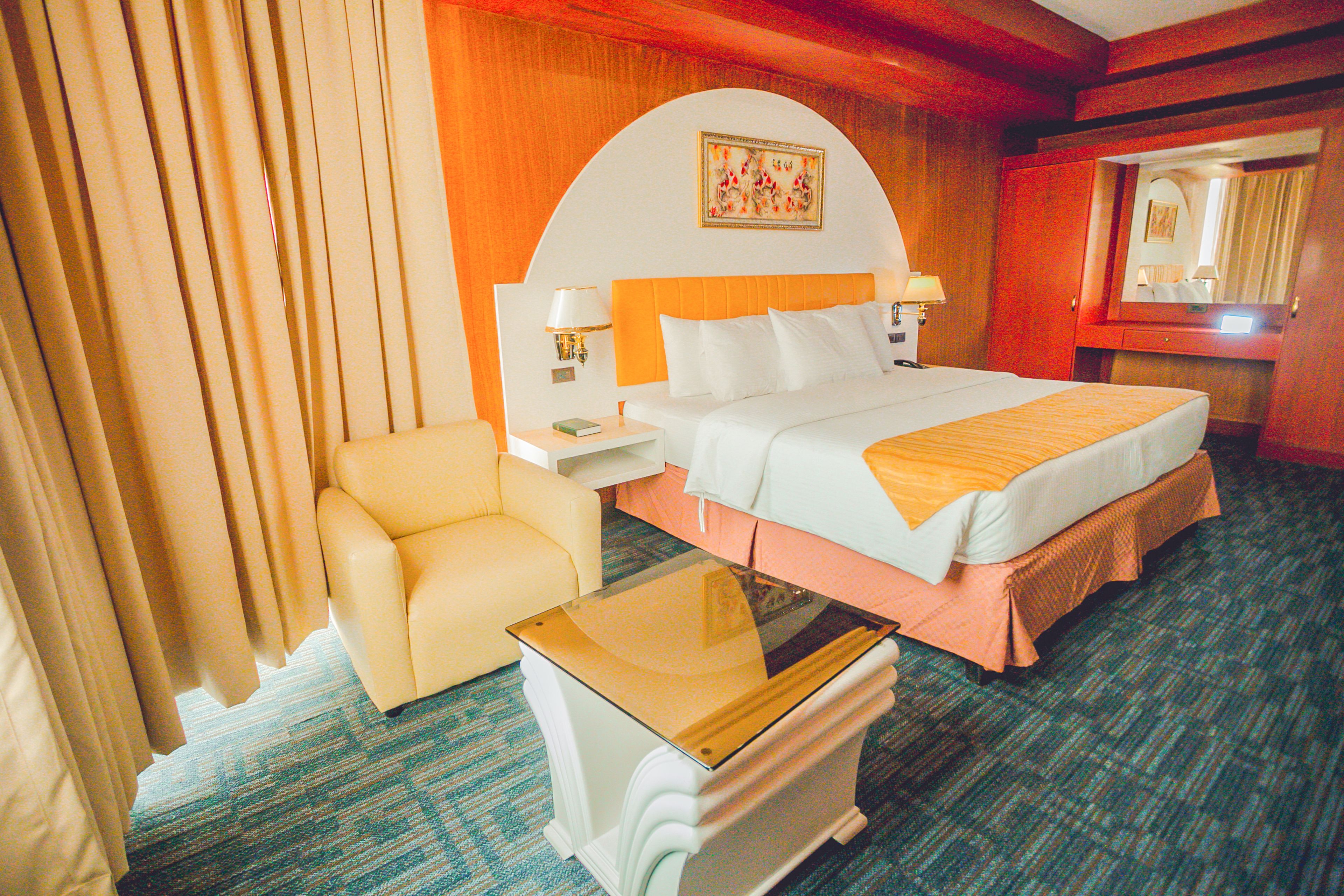 A hotel room with a bed, a chair, a nightstand, and a table.