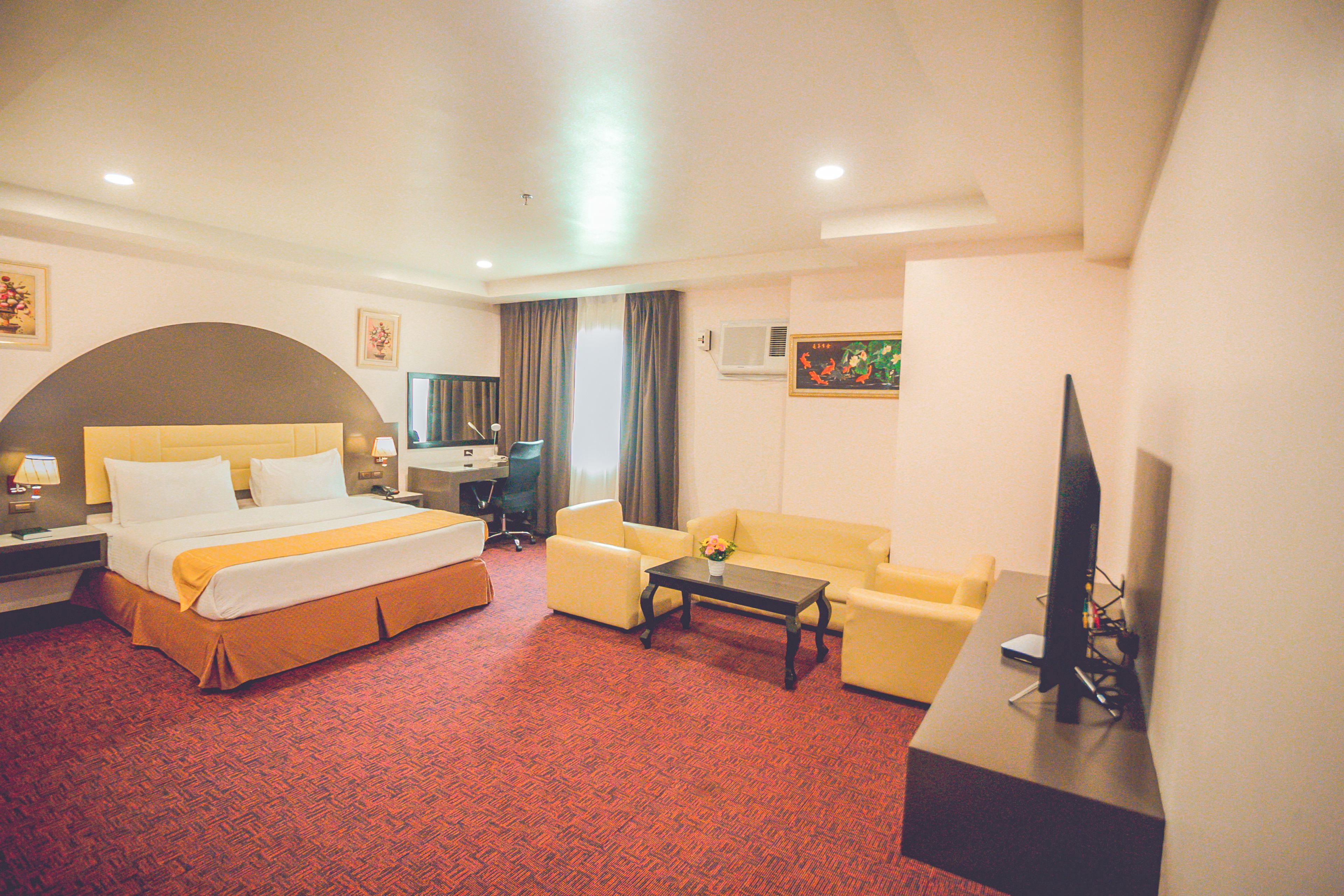 A hotel room with a bed, a sofa, a desk, and a TV.