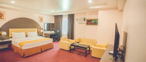 A hotel room with a bed, a sofa, a desk, and a TV.