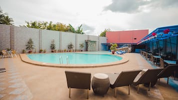 Relax by the resort pool surrounded by lounge chairs and a bar area, with a palm tree and potted plants nearby.