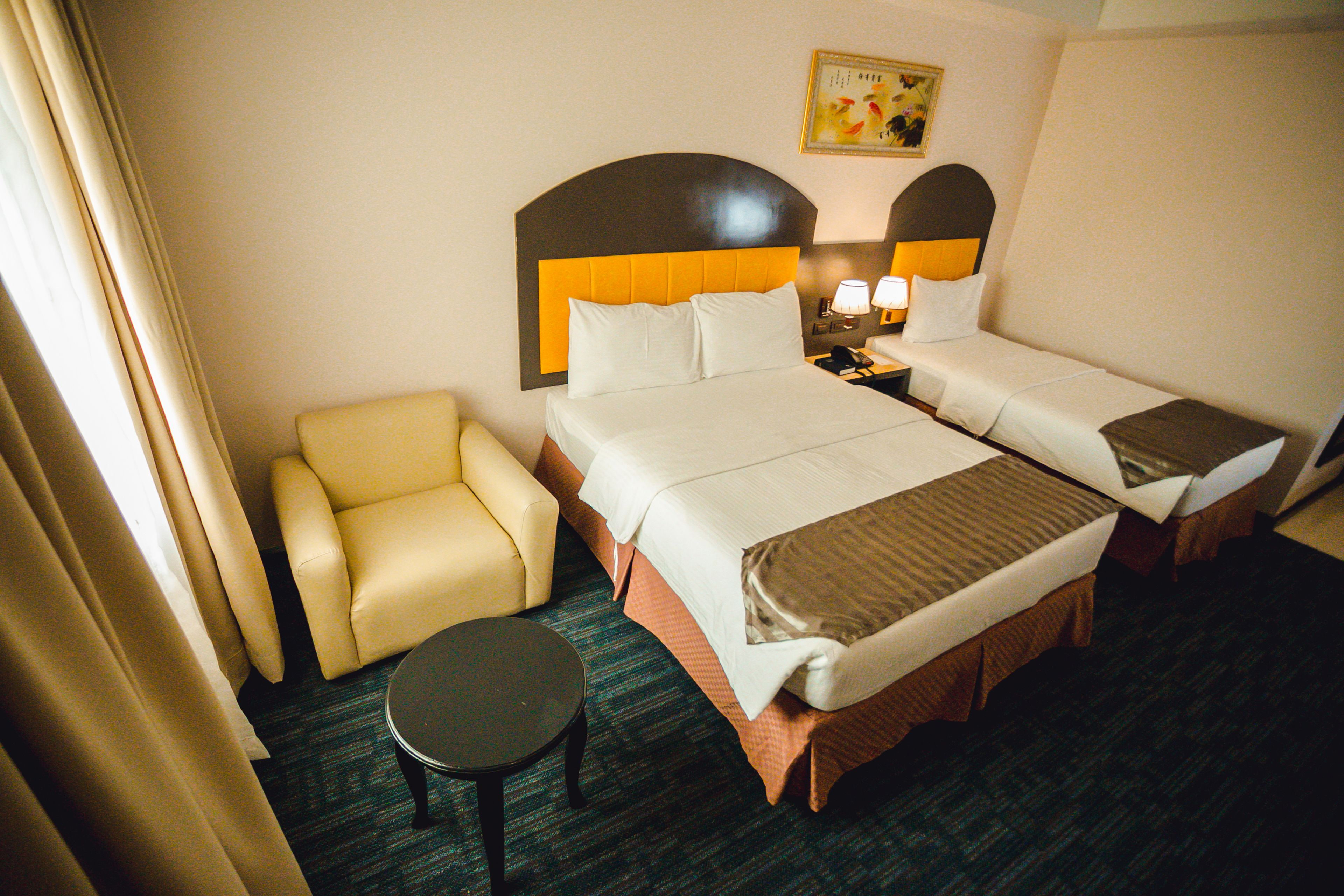 A hotel room with two beds, a chair, a small table, and a nightstand with lamps.