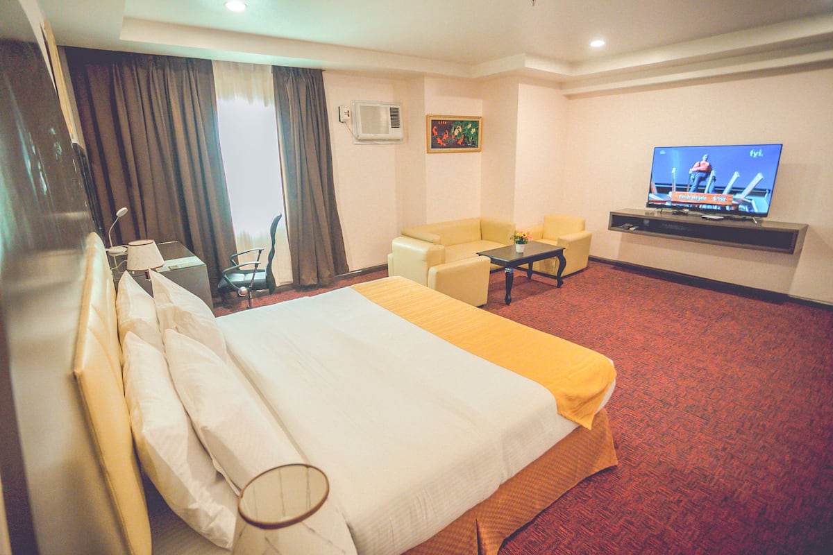 A hotel room with a large bed, a television, a desk, and a sofa.