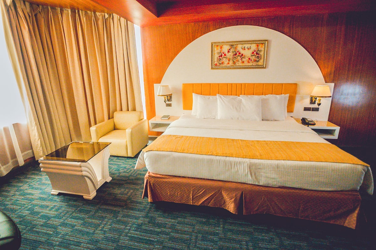 A hotel room with a large bed, two bedside tables with lamps, a chair, and a small table.