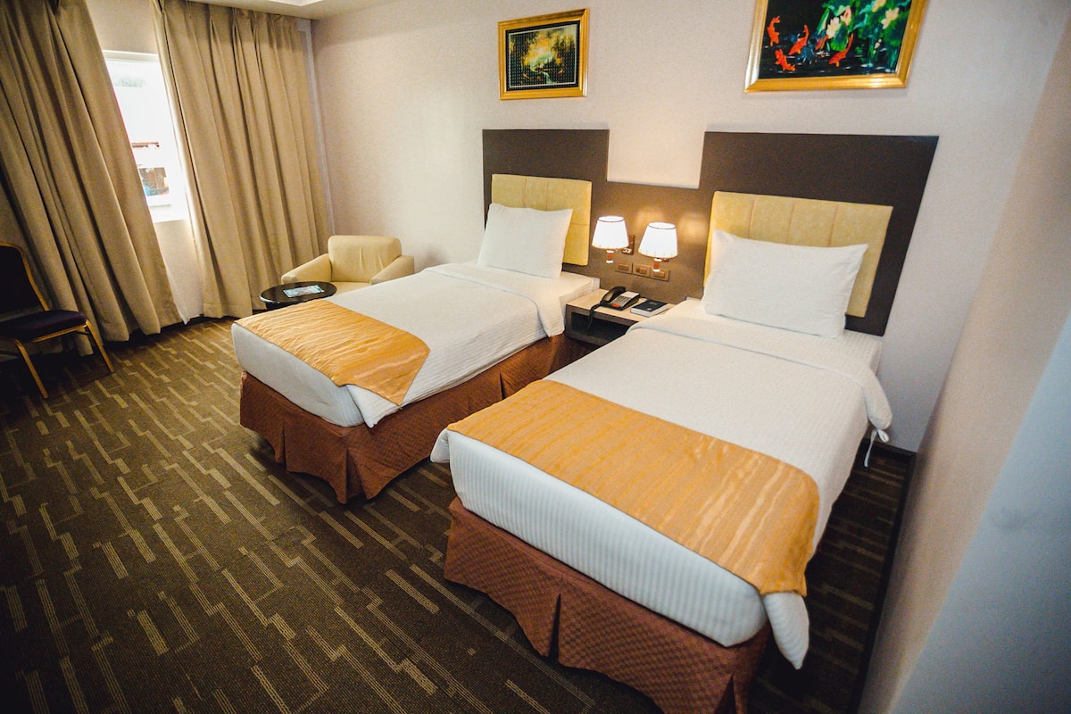 A hotel room with two beds, a chair, a desk, and a telephone.