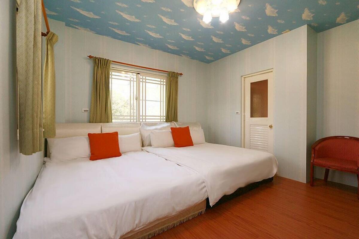 Una habitación con dos camas, una ventana con cortinas, una puerta y una silla.