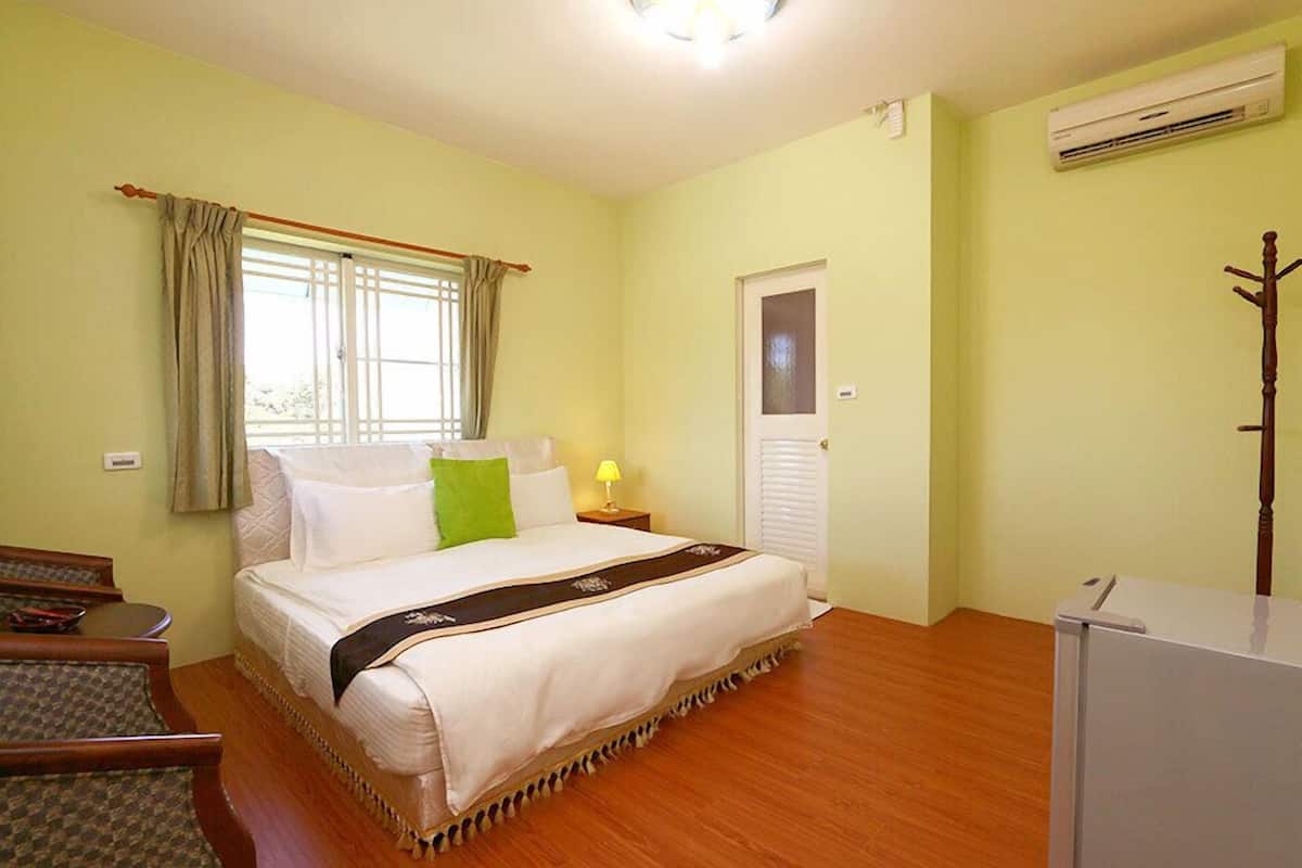 Una habitación de hotel con cama, mesita de noche, lámpara, armario y ventana con cortinas.