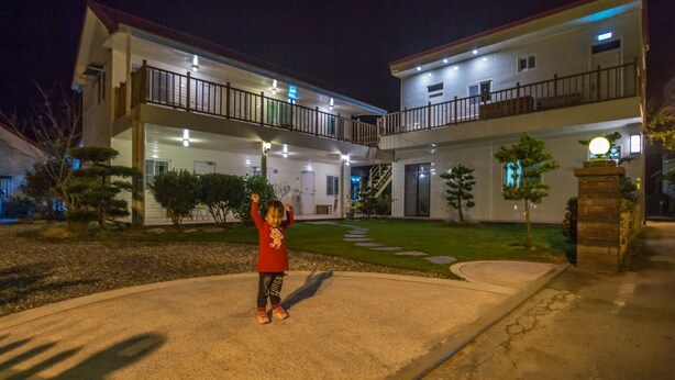 A two-story building with a balcony on the upper floor, a well-maintained lawn, and a child playing in the driveway. - YUAN QI WU Homestay (Shoufeng)