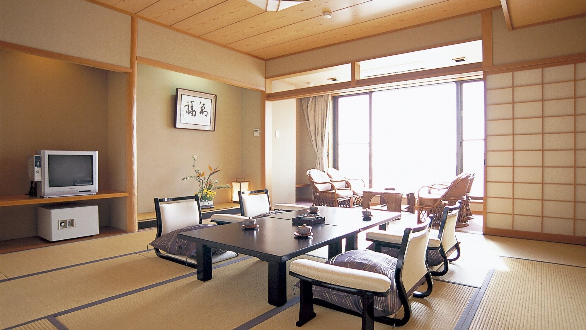 Una habitación japonesa tradicional con suelo de tatami, una mesa baja, sillas, un televisor y un cuadro en la pared.