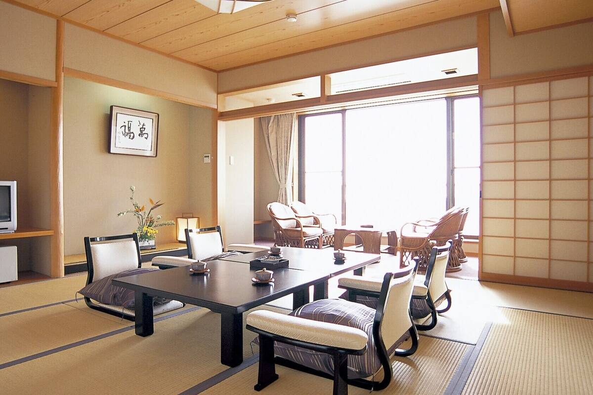 Una habitación japonesa tradicional con suelo de tatami, una mesa baja, sillas, un televisor y un cuadro en la pared.