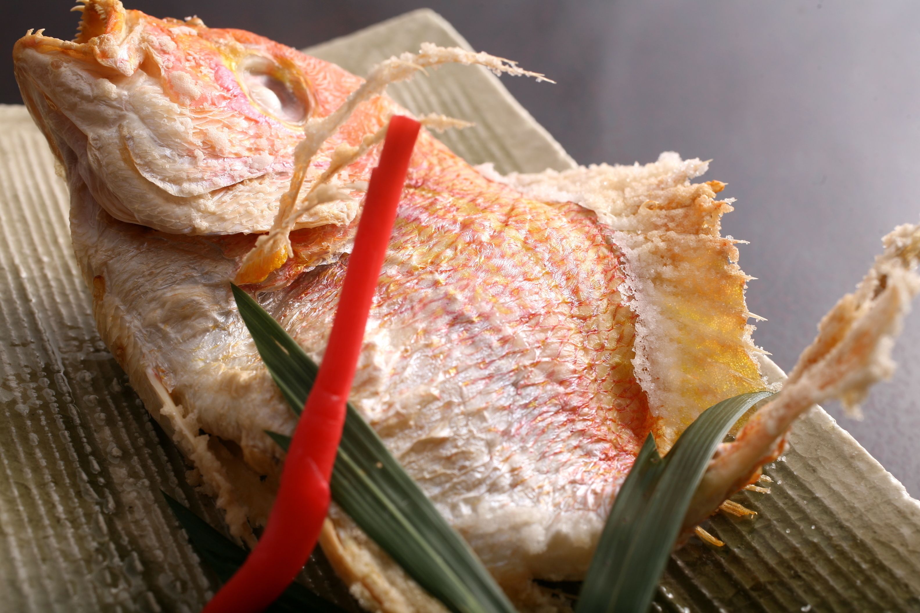 A fish with crispy skin and a red garnish on a textured surface.