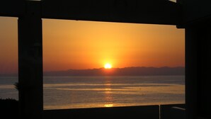 Une vue sur le coucher de soleil depuis un espace extérieur aménagé, abrité, avec une table et des chaises au premier plan.