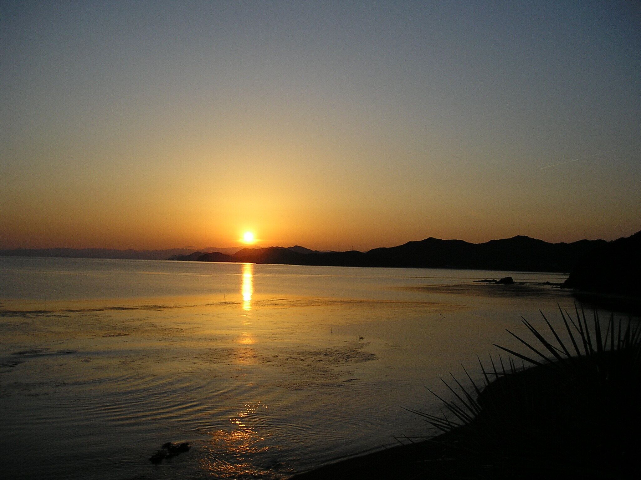 A sunset over a calm body of water with distant mountains.