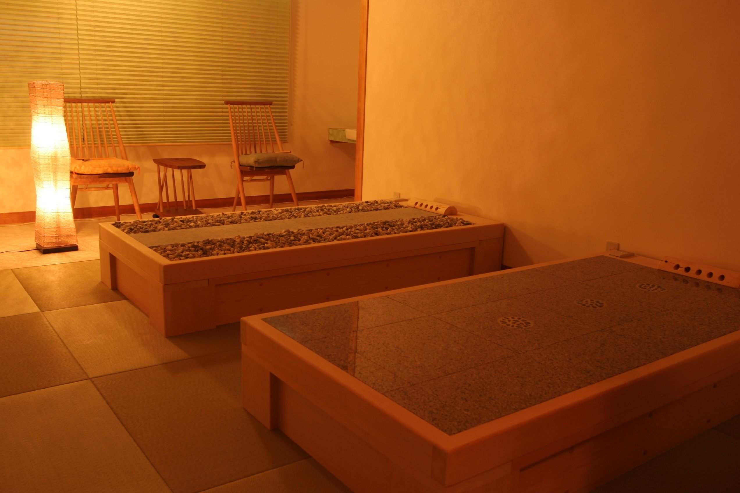 A room with two wooden beds, a small table, two chairs, and a floor lamp.
