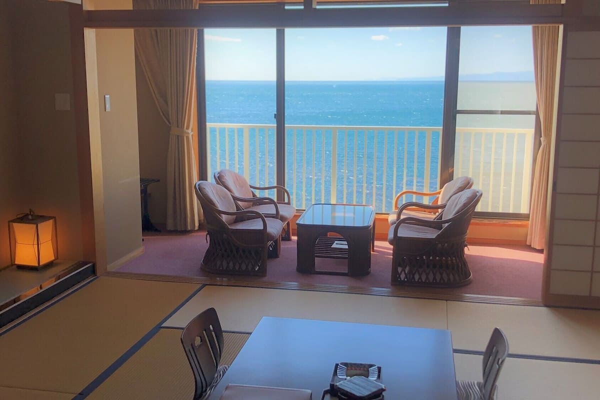 A room with a view of the sea, two wicker chairs, a small table, and a floor lamp.