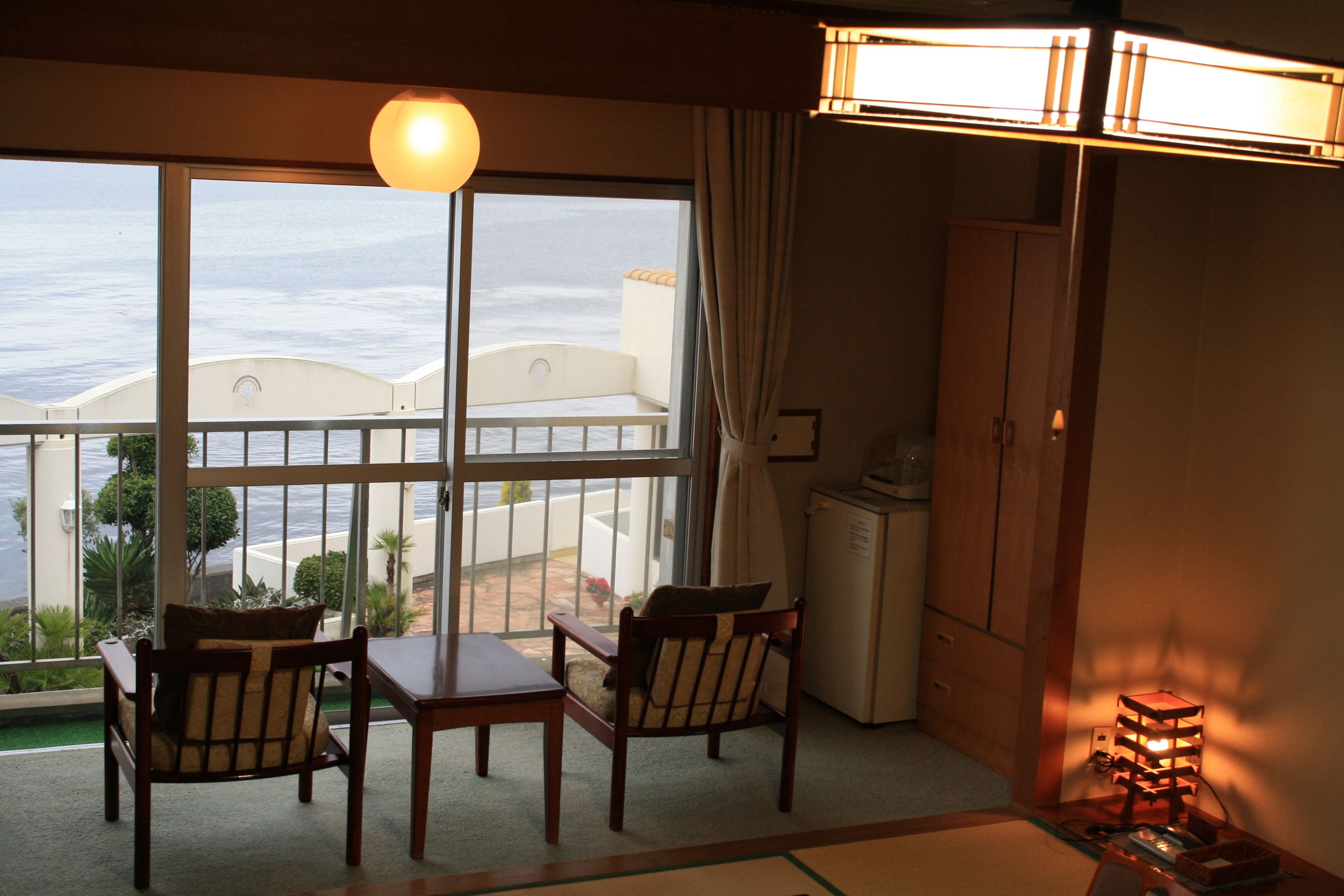 Une pièce avec un balcon donnant sur un plan d’eau, une table à manger avec des chaises, un buffet et une lampe sur pied.