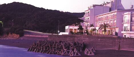 A coastal hotel with a beach view, a pool area, and a mountain backdrop.