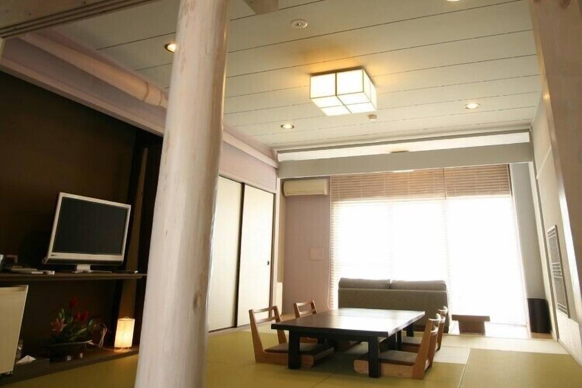 Una habitación con una mesa de comedor, sillas, un televisor sobre un mueble bajo y un pilar grande.