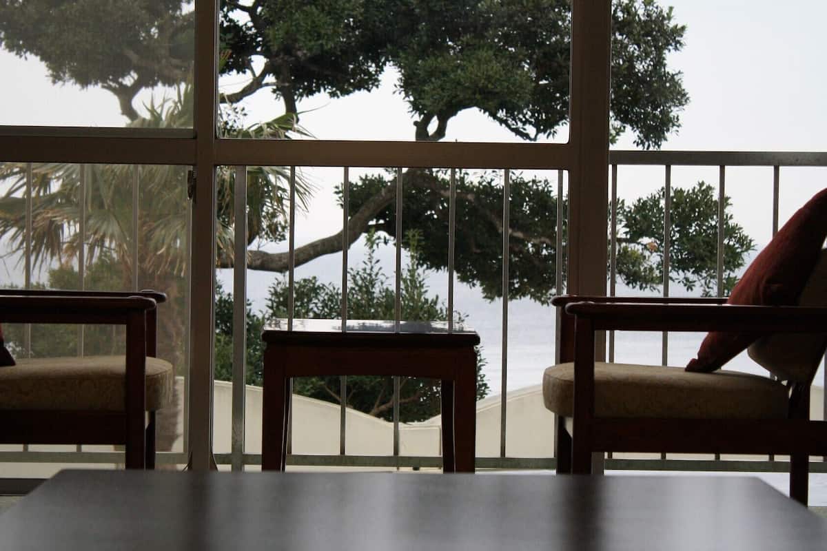 A room with two chairs and a table, large windows with a view of trees and a building.