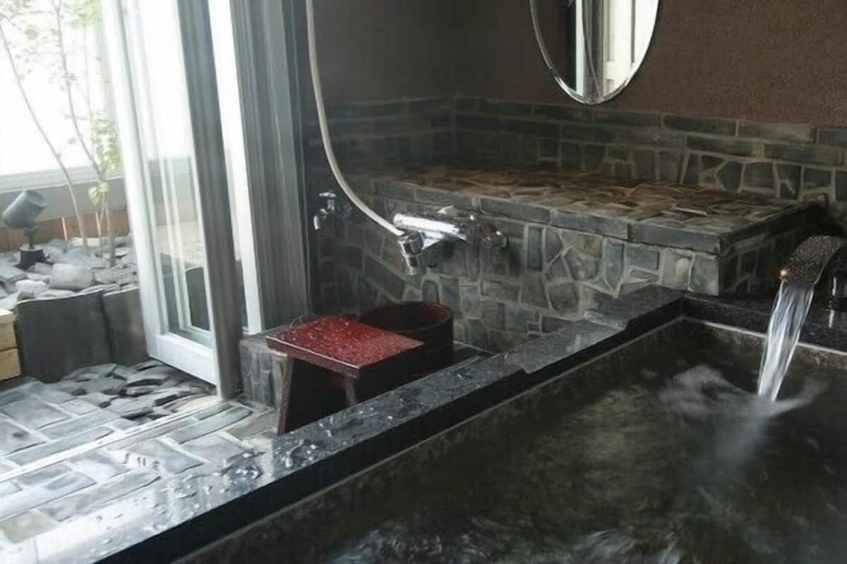 A spa area with a stone-tiled floor, a hot tub, and a mirror on the wall.