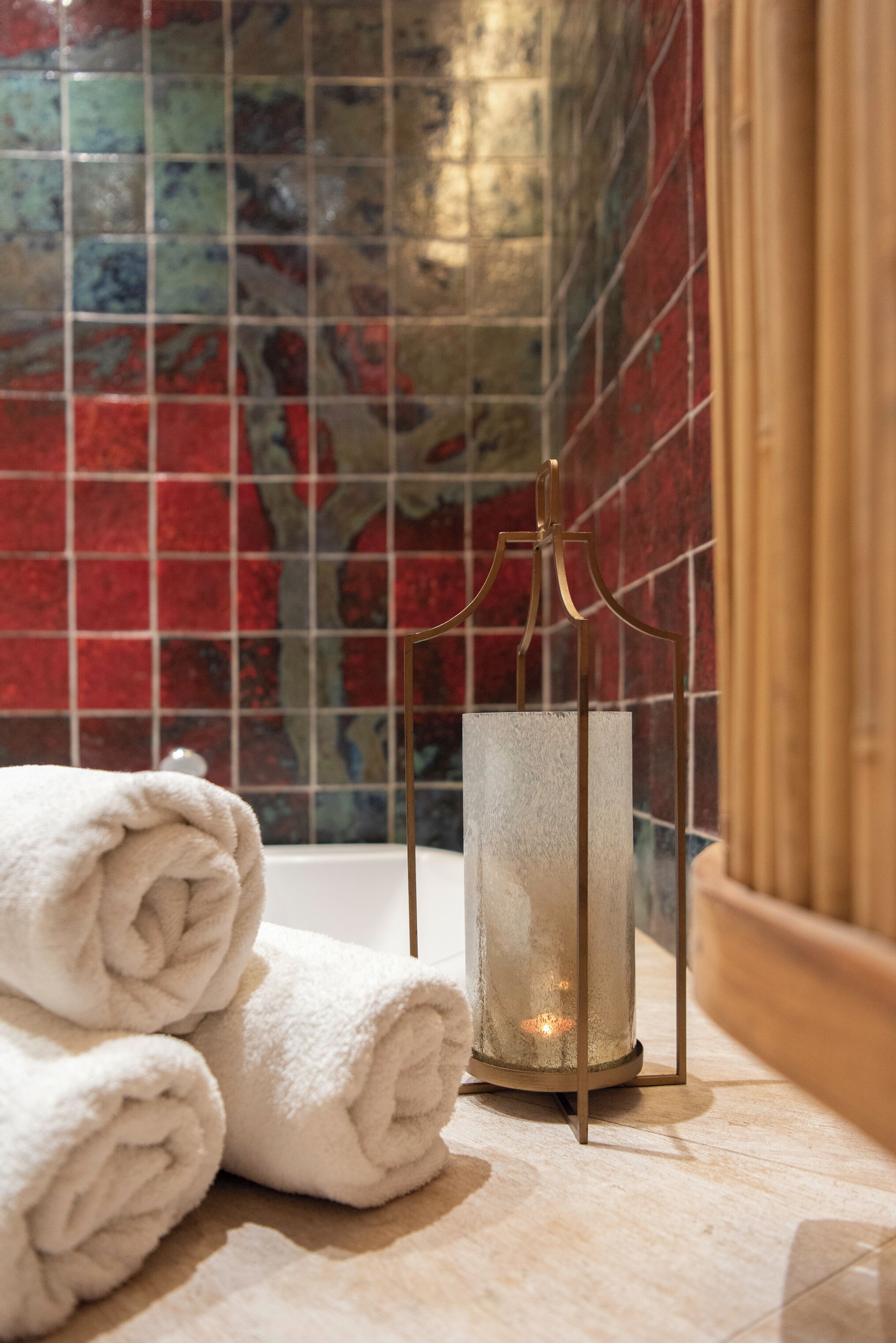 A bathroom with a tiled wall, a glass-topped bathtub, and a towel rack with folded towels.