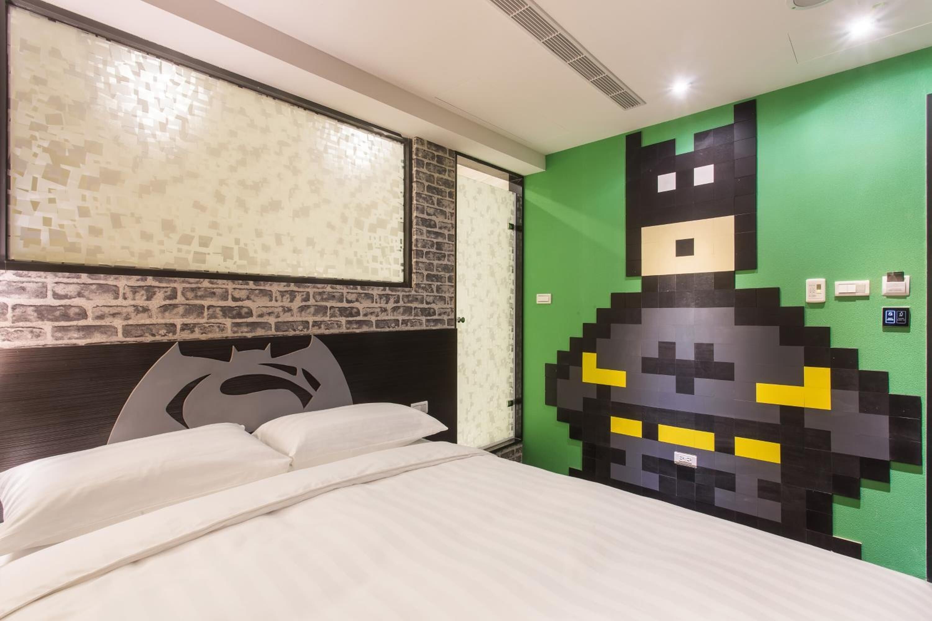 A room with a bed, a green wall with a pixelated design, a brick-patterned wall, and a window with a textured blind.