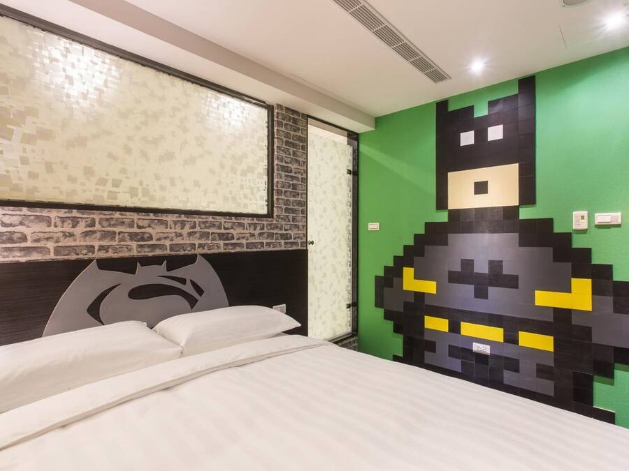 A room with a bed, a green wall with a pixelated design, a brick-patterned wall, and a window with a textured blind.