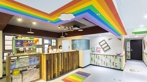 A brightly colored reception area with a wooden counter, a play area with toys, and a white brick wall with artwork. - Rf Hotel - Sanchung (New Taipei City)