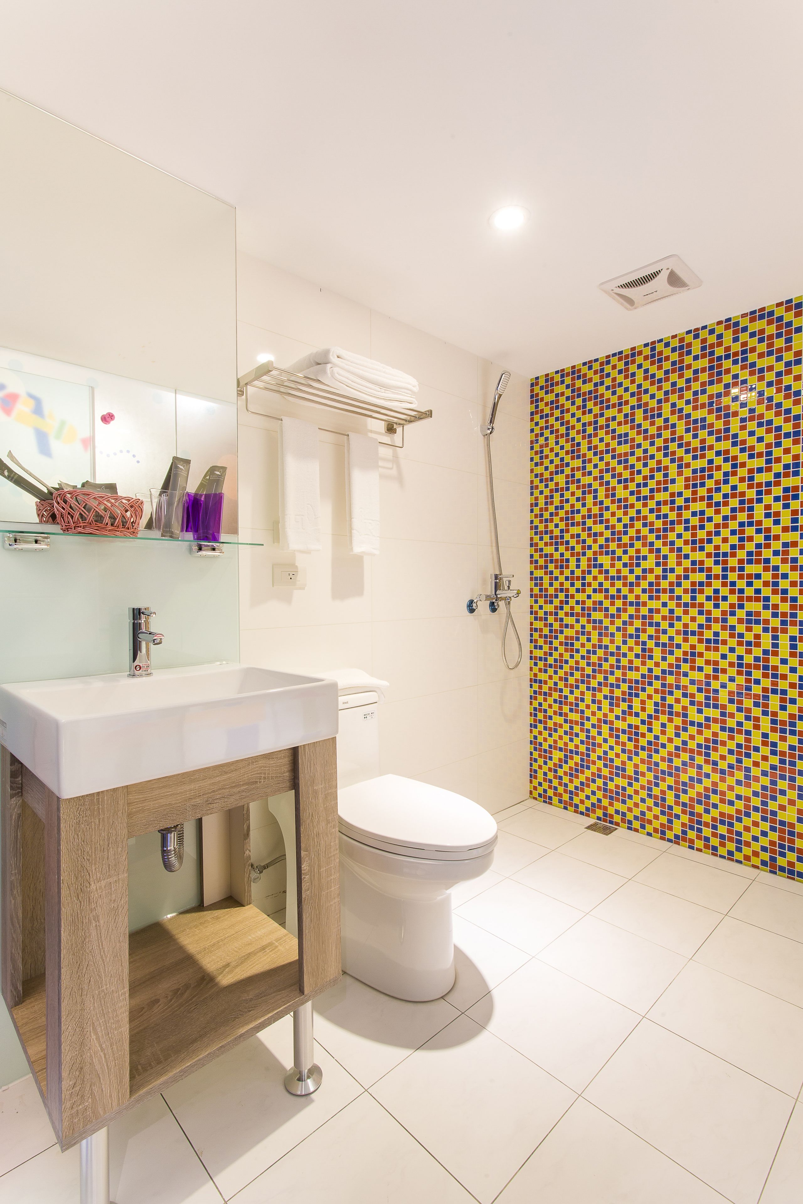 A bathroom with a white sink, mirror, and toilet. There is a shower area with a colorful mosaic wall.