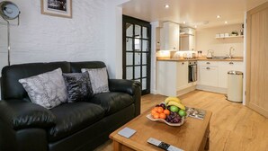 A modern living room with a black leather sofa, a wooden coffee table with fruit, and a remote control. - The Weary Friar (Saltash)