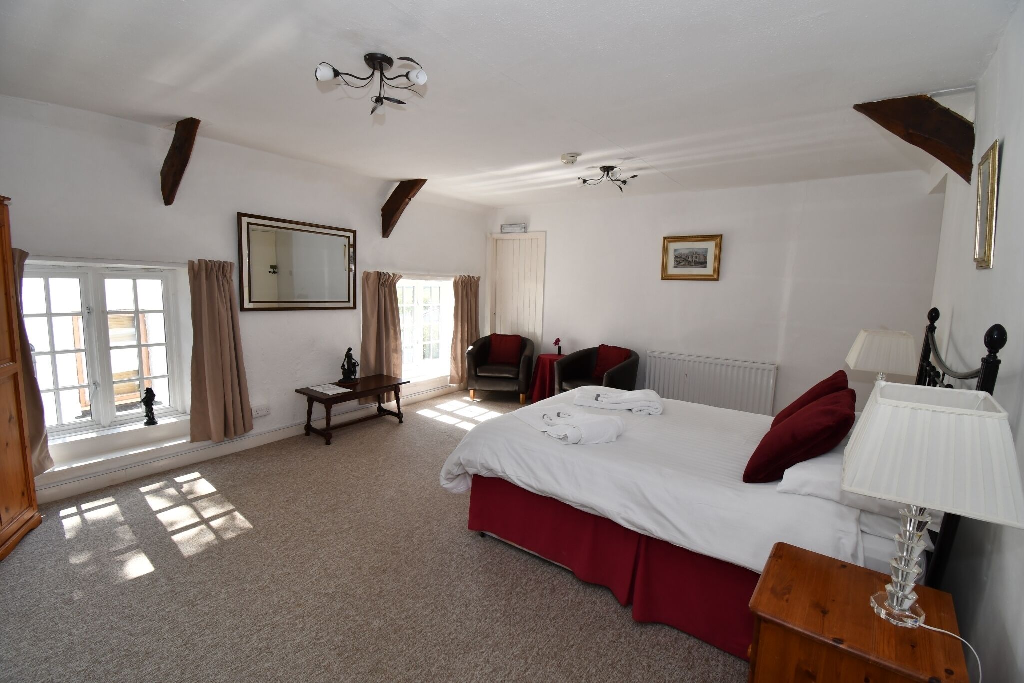 A hotel room with a large bed, a desk, a chair, a window with curtains, and a ceiling fan.