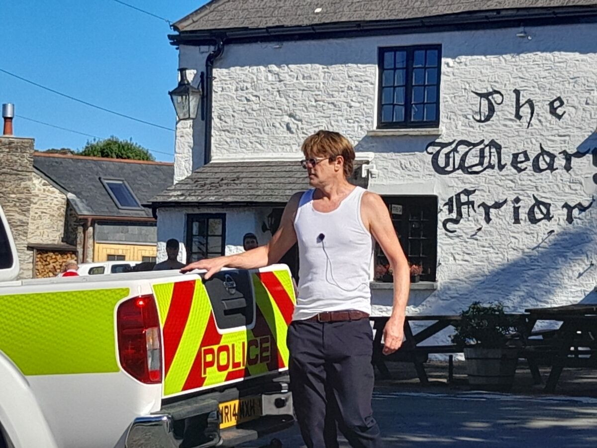 Une personne se tient à côté d’un véhicule de police, un panneau indiquant « POLICE » étant placé devant un bâtiment sur lequel on peut lire « The Merry Friar ».