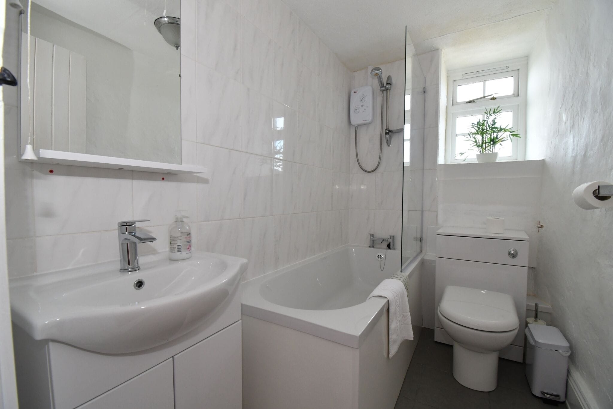 A modern bathroom with a sink, bathtub, toilet, and a window with a plant.