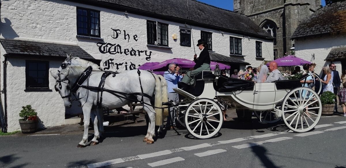 Un carruaje tirado por caballos blancos frente al pub The Merry Grid.