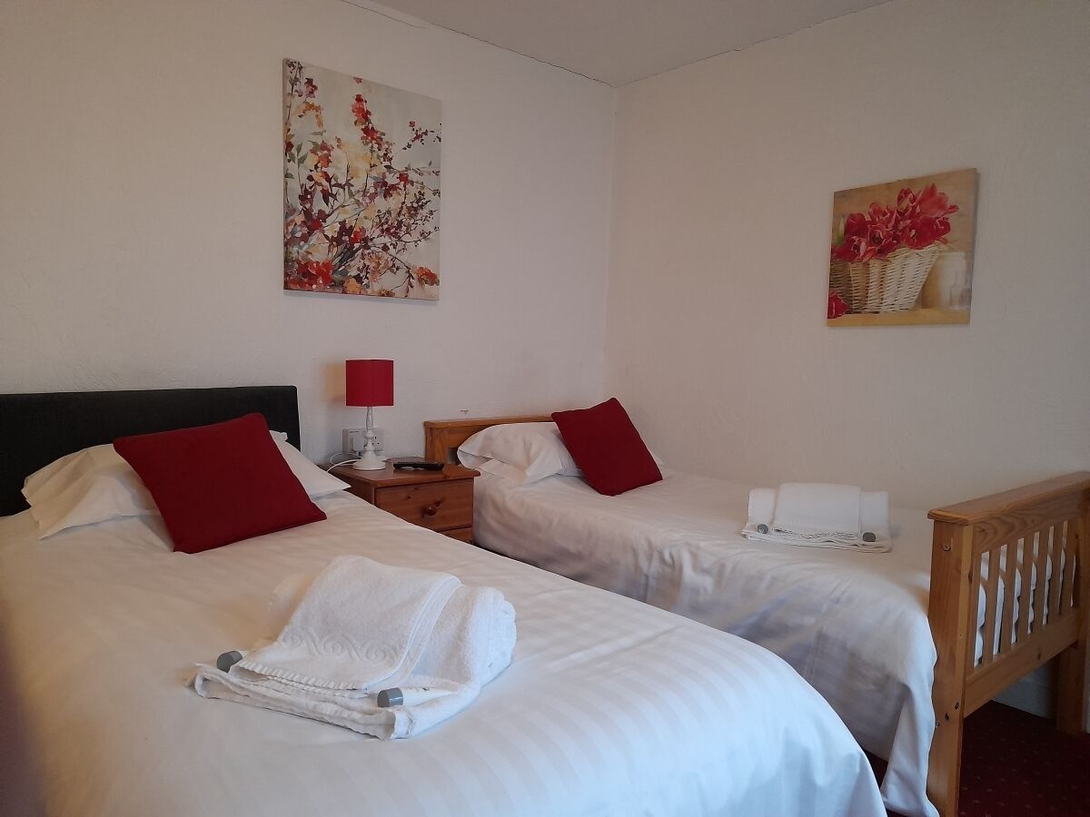 Une chambre d’hôtel avec deux lits, chacun agrémenté de draps blancs et d’oreillers rouges, une table de chevet avec une lampe et des œuvres d’art accrochées aux murs.