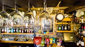 A bar area with multiple hanging glassware, a cash register, and shelves with bottles and snacks. - The Weary Friar (Saltash)