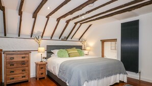 A bedroom with a wooden ceiling, a bed with a grey and white bedspread, two bedside tables with lamps, and a radiator. - The Weary Friar (Saltash)