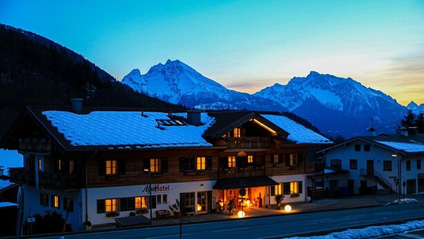 Een hotel met een sneeuwbedekte dak, een balkon en een berg op de achtergrond.
