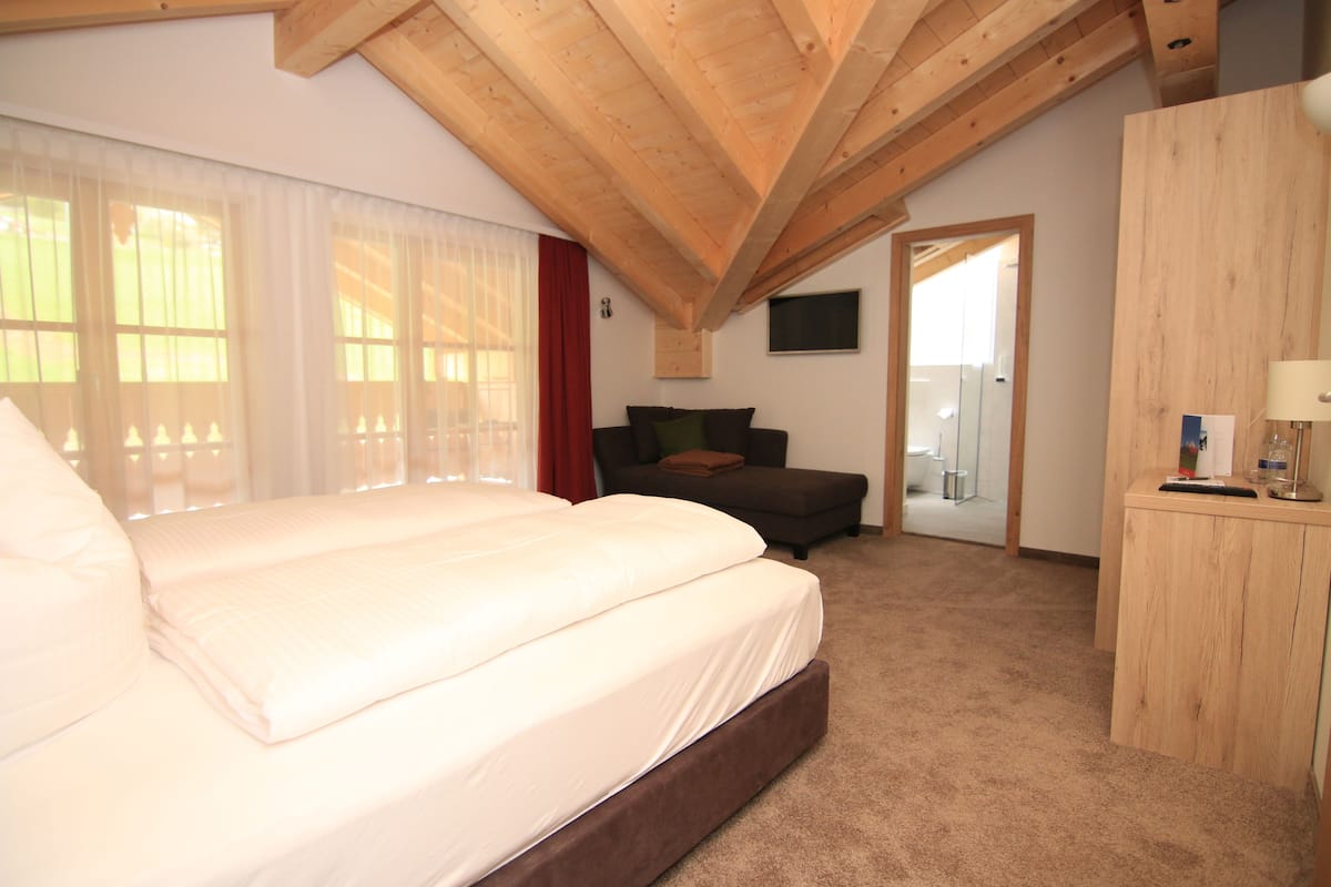 Um quarto com uma cama grande, teto de madeira, sofá, televisão e escrivaninha.