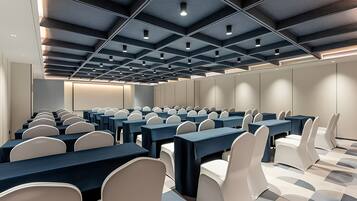 A conference room with rows of tables and chairs, a modern ceiling design, and a neutral color scheme.