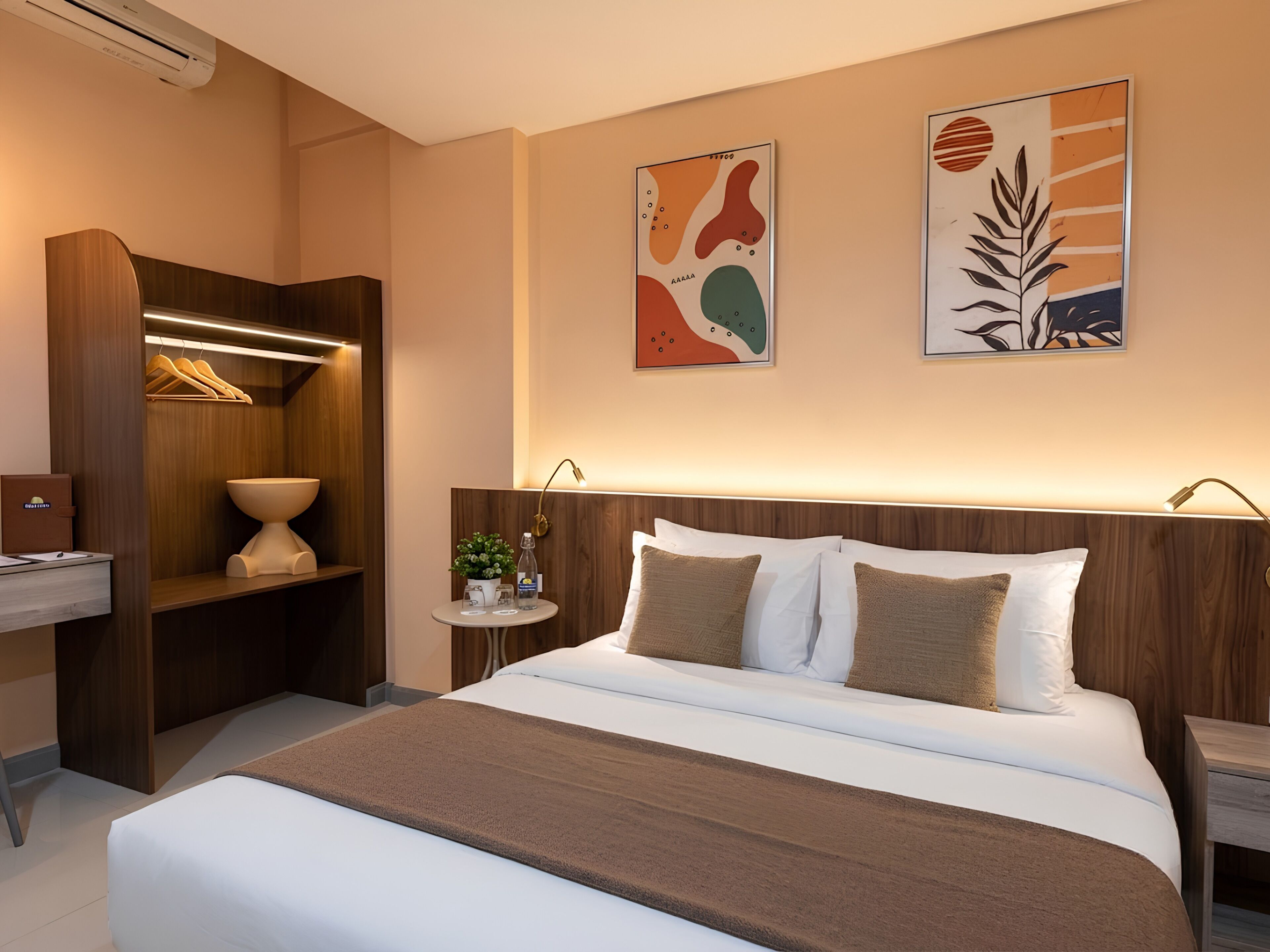 Habitación de hotel con cama, mesitas de noche, armario de madera, una pequeña mesa redonda con una planta y arte abstracto en la pared.