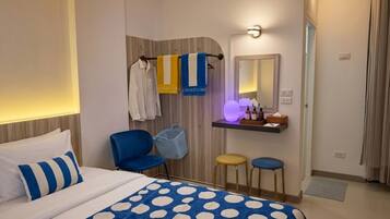 Una habitación de hotel con una cama, una silla, un taburete, una tocador con espejo y un perchero para toallas.