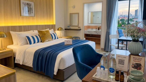 Een hotelkamer met een bed, nachtkastjes, een bureau met een vaas, een spiegel en uitzicht op de stad.