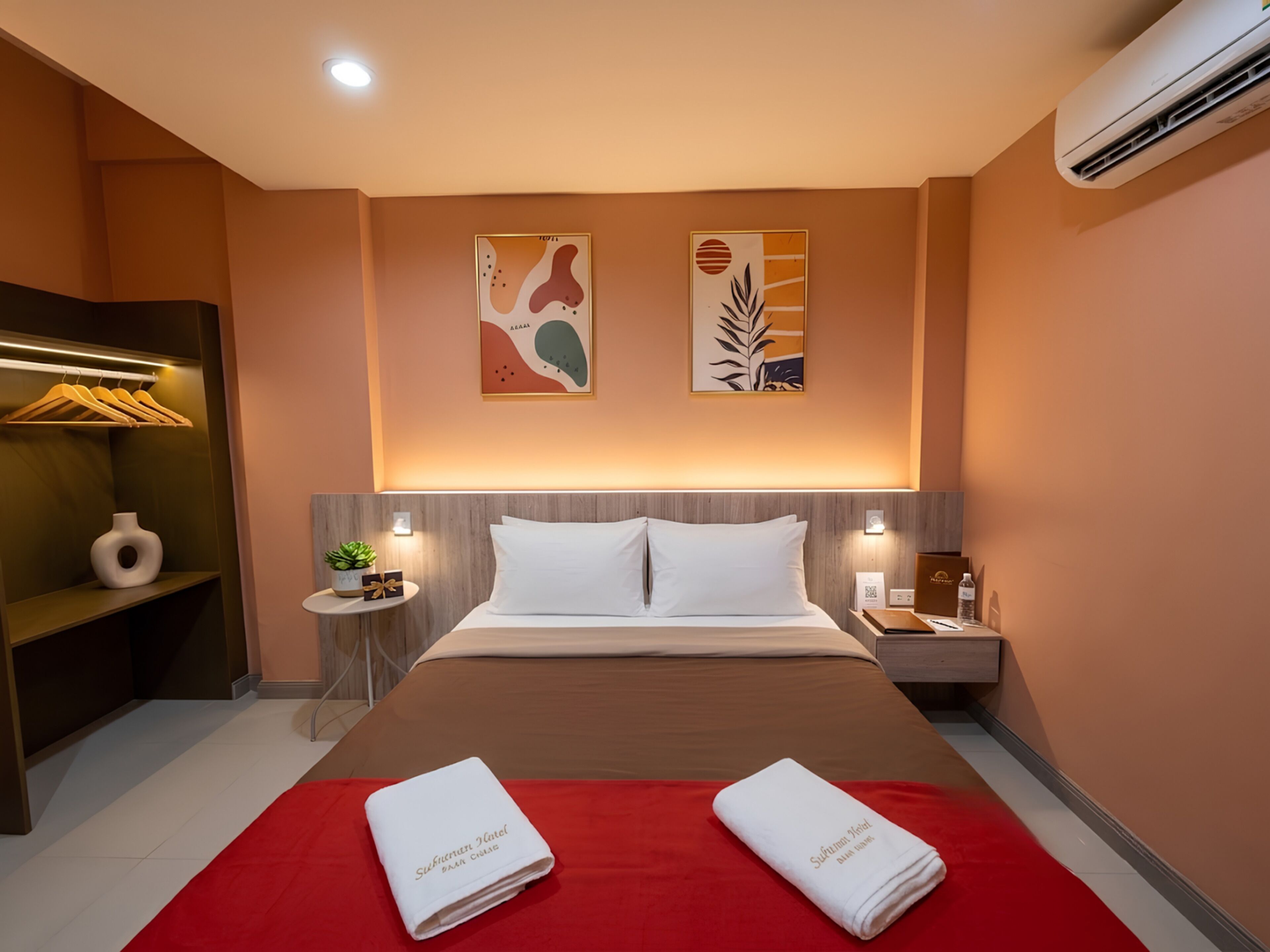 A hotel room with a bed, a nightstand, a red throw blanket, and two towels.