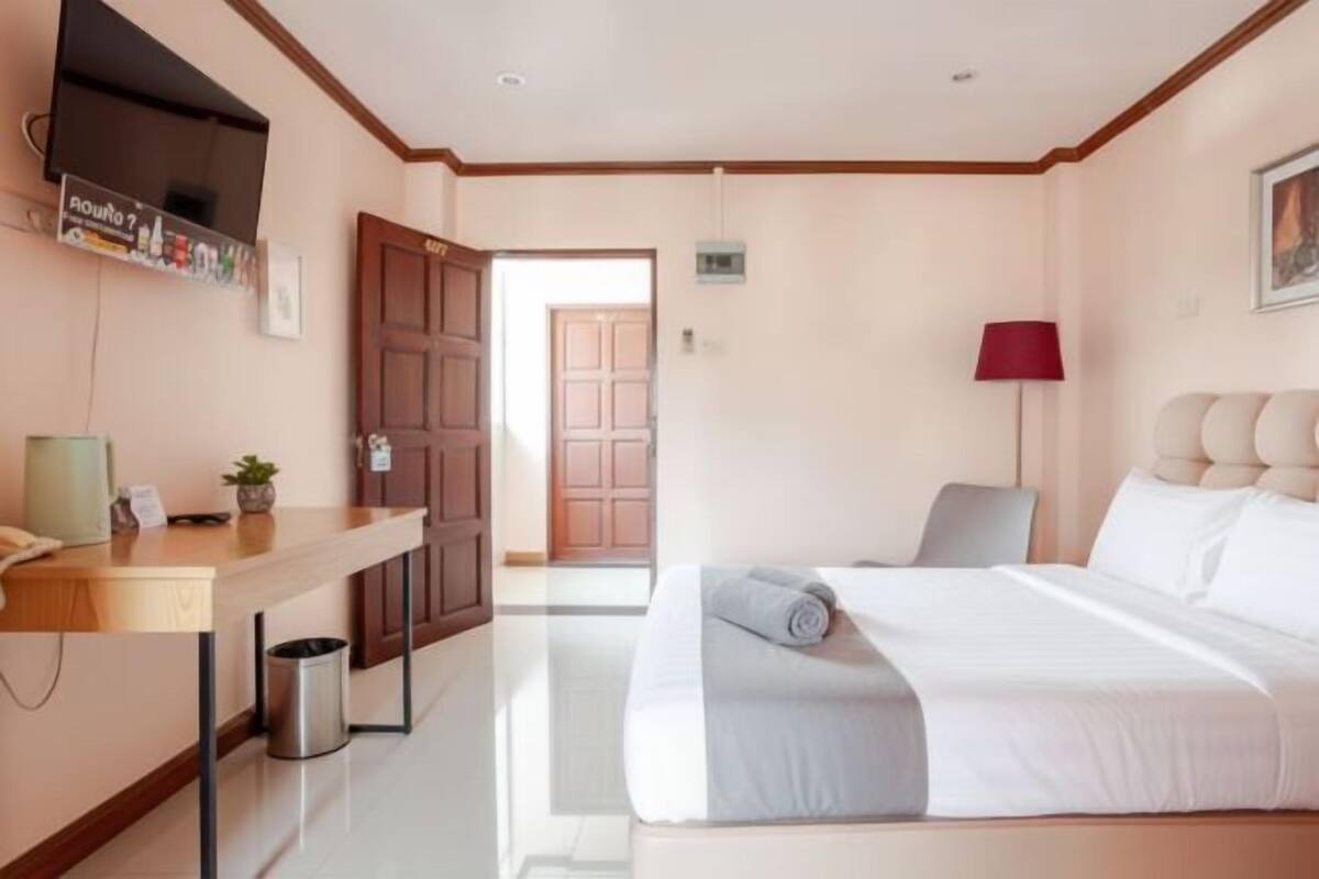 Habitación de hotel con cama, escritorio, silla, televisor, lámpara y puerta que da a otra habitación.