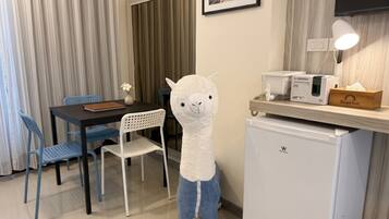 Habitación de hotel con comedor, un refrigerador pequeño, una lámpara y un peluche.