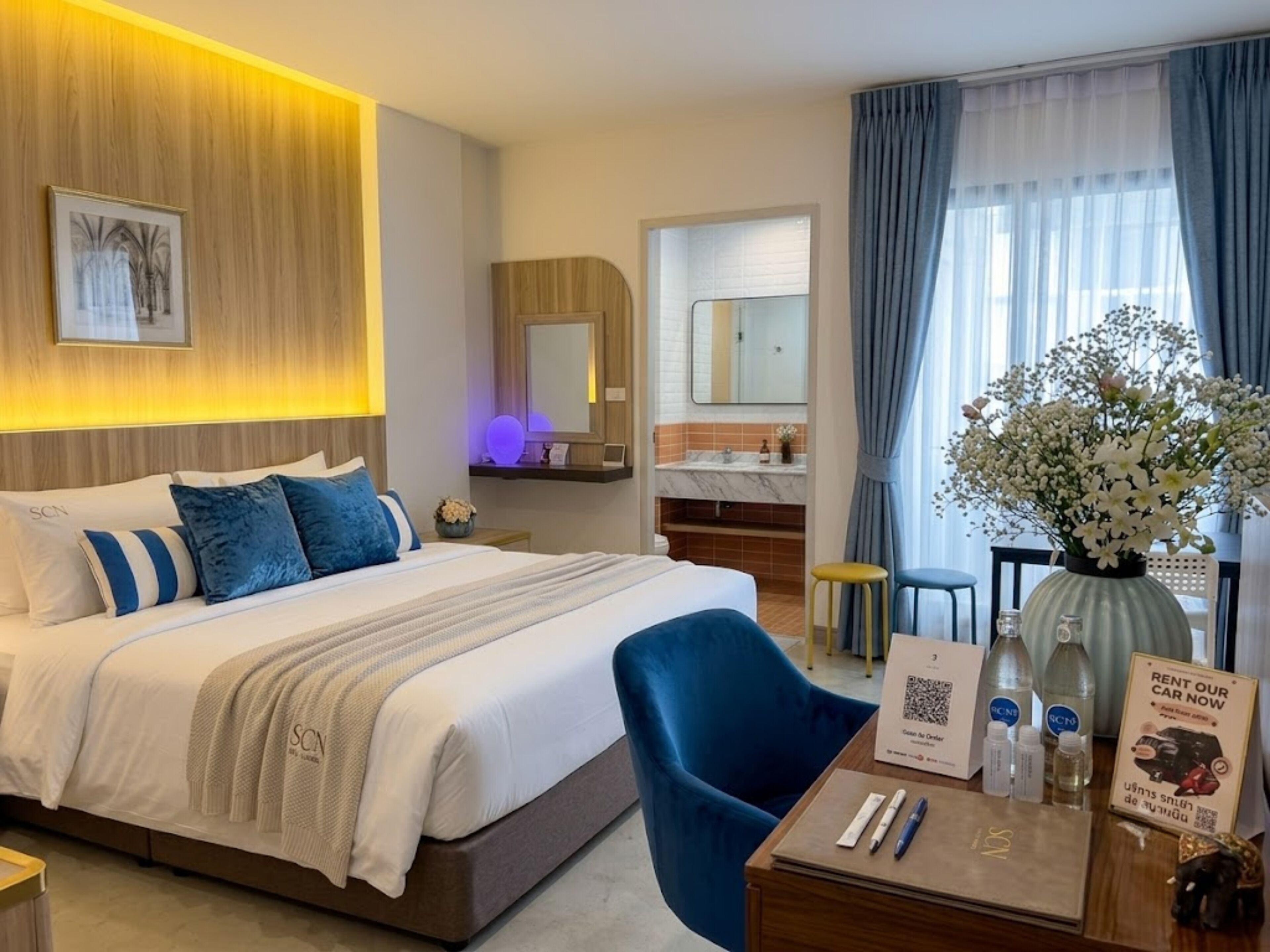 Habitación de hotel con cama, escritorio con silla, baño y vistas al exterior.